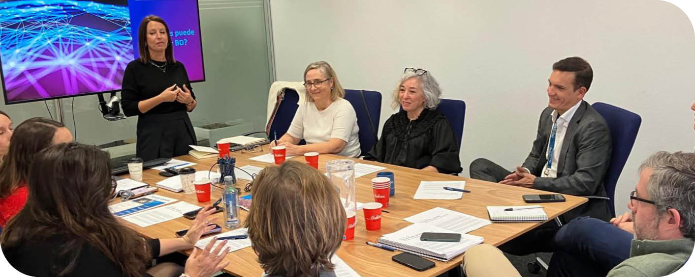 A group of people are sitting around a table, engaged in a meeting. There are several cups and a cell phone on the table. A TV is visible in the background. AI generated content