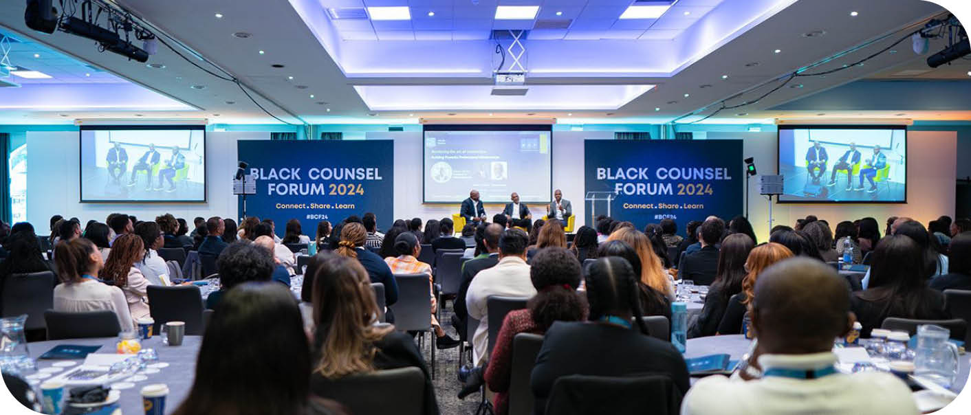 A large group of people are seated in a conference room, watching a presentation on a large screen. The audience is engaged and focused on the speaker. The room is equipped with a projector and a laptop, and there are several chairs and dining tables scattered throughout the space. The attendees are dressed in business attire, indicating a professional setting. AI generated content