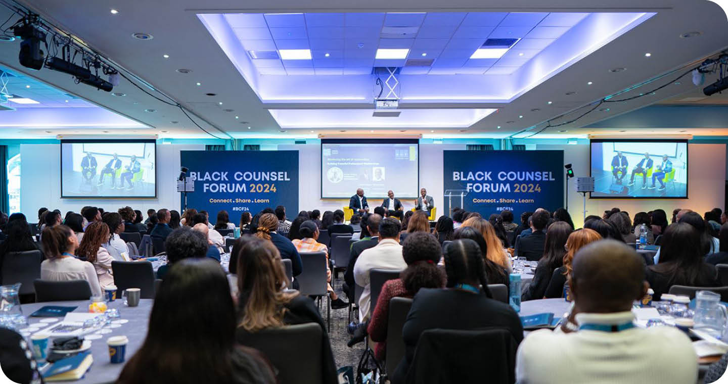 A large group of people are seated in a conference room, watching a presentation on a large screen. The audience is engaged and focused on the speaker. The room is equipped with a projector and a laptop, and there are several chairs and dining tables scattered throughout the space. The attendees are dressed in business attire, indicating a professional setting. AI generated content